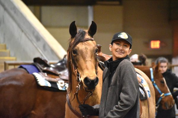 A male student smiles while holding a horse.