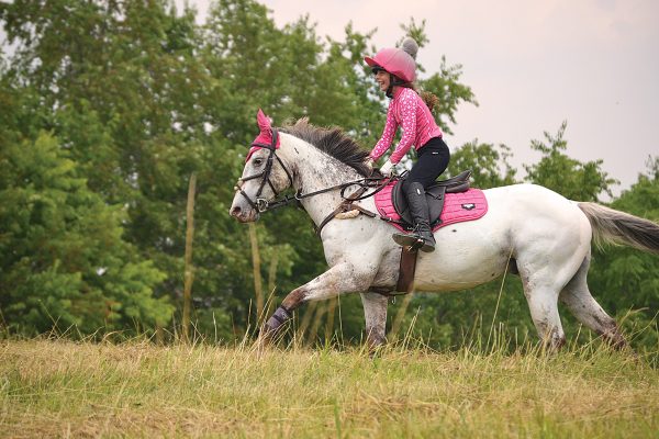 A young equestrian galloping her pony in a field.