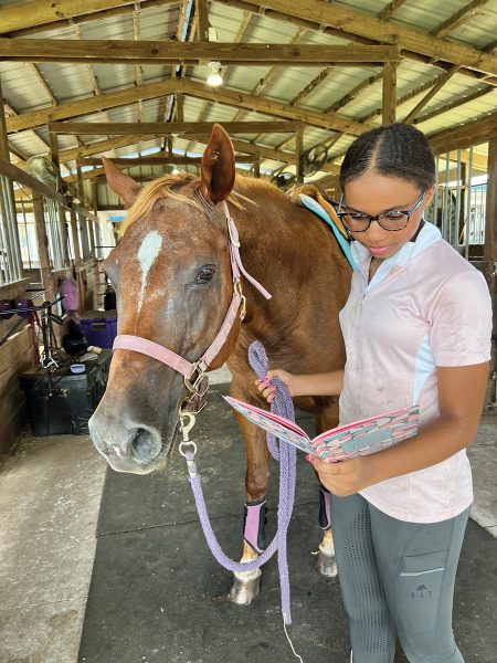 A riding student looks at her riding lesson diary while holding her horse.