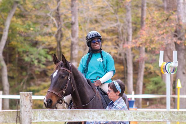 A student smiles aboard a therapeutic riding horse